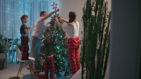 Happy-family-preparing-for-New-Year-winter-holidays-celebration-concept.-Young-30s-couple-his-preschool-adorable-two-sons-decorating-Christmas-tree-create-festive-mood-atmosphere-at-modern-cozy-house.-High-quality-4k-footage